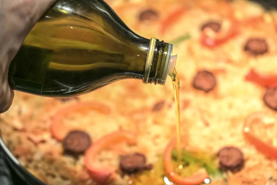 Chorro de aceite de oliva vertido desde una botella de vidrio sobre una pizza