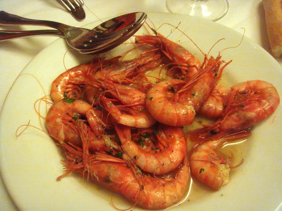 Camarones enteros cocidos, de color rosado anaranjado, servidos en un plato con cubiertos