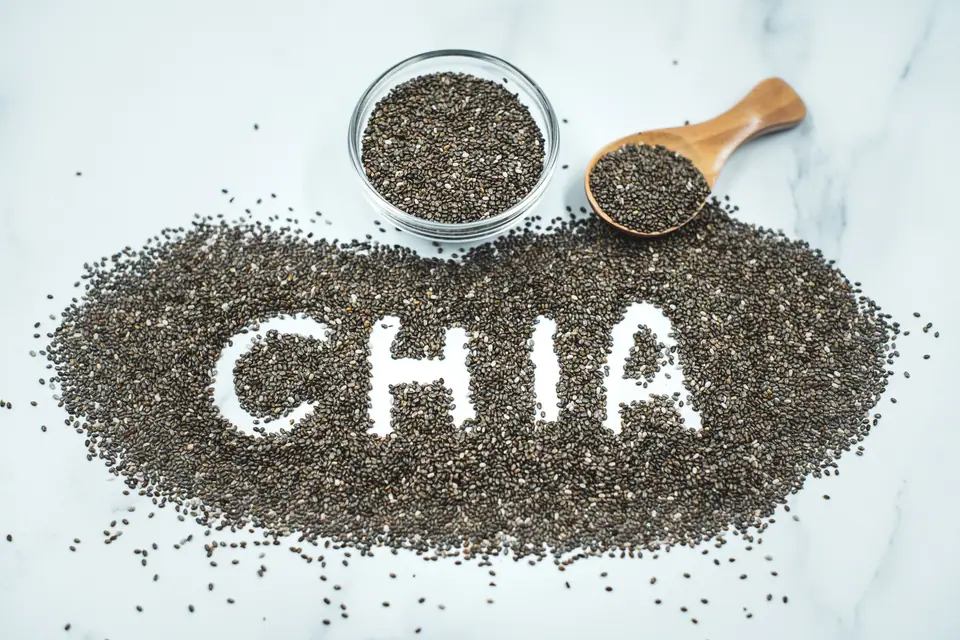 Semillas de chía en un bol de vidrio y una cuchara de madera, con la palabra chía escrita sobre las semillas