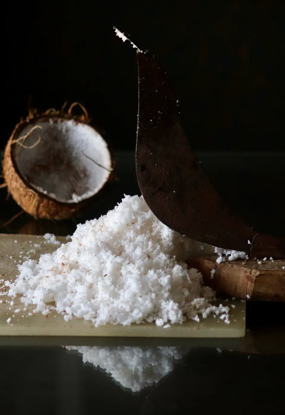 Montón de coco rallado sobre una tabla junto a medio coco abierto
