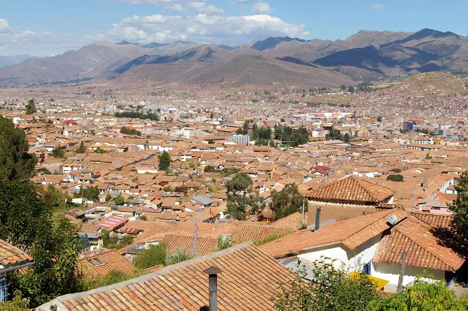 Vista de Cusco con techos de teja rojiza y montañas al fondo bajo cielo azul