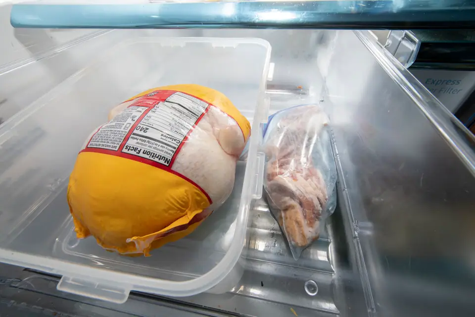 Ave entera envasada y un paquete de carne dentro de un recipiente plástico en el estante de la heladera