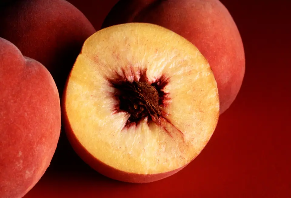 Duraznos enteros y uno cortado al medio que muestra el carozo