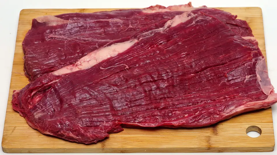 Dos piezas de flank steak (vacío/bavette) crudas sobre una tabla de madera