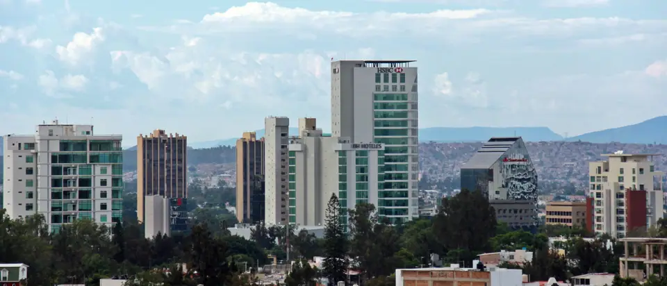 Edificios altos de Guadalajara entre árboles, con cerros al fondo
