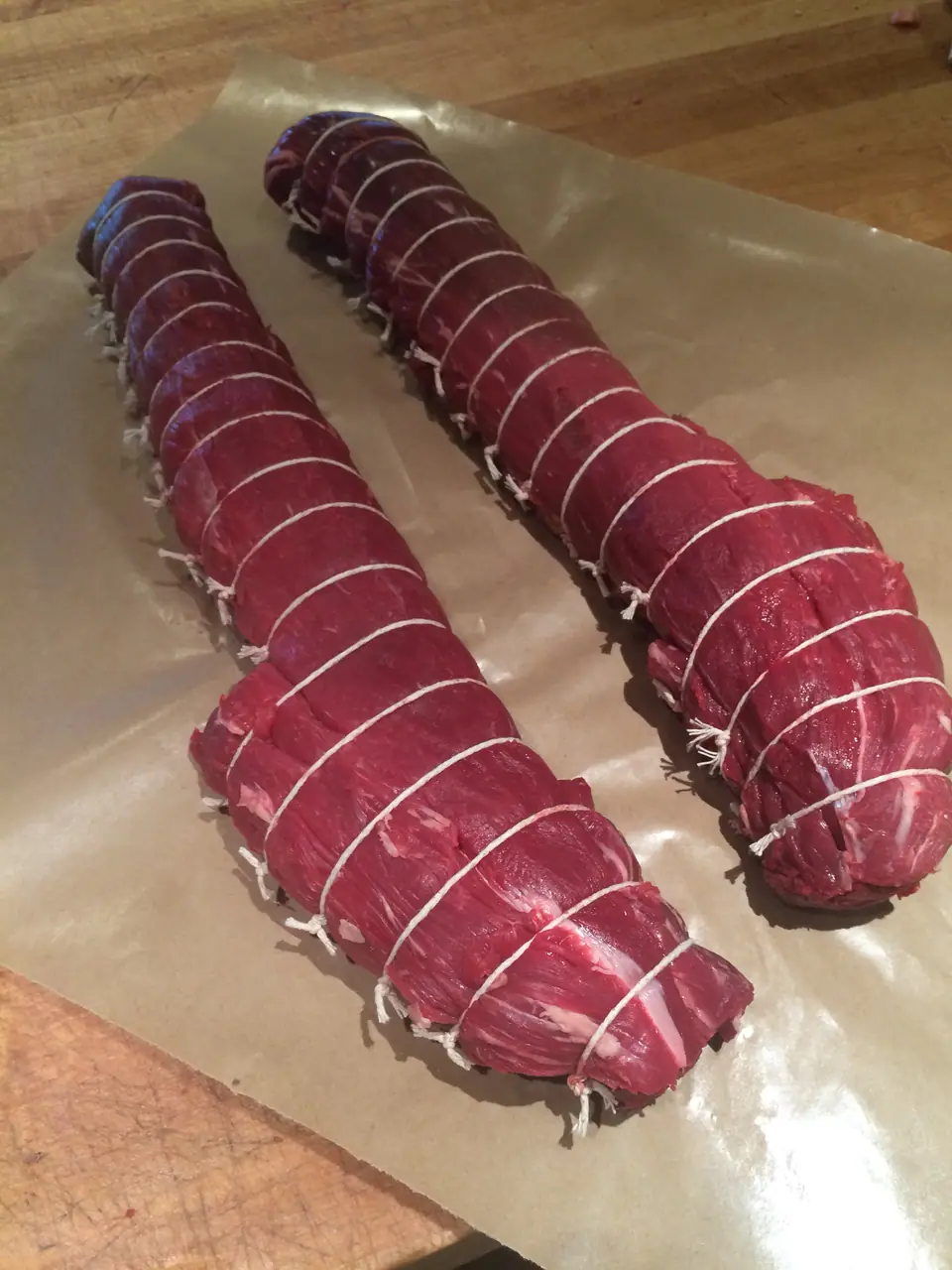 Dos piezas de lomo de res crudo atadas con hilo sobre papel