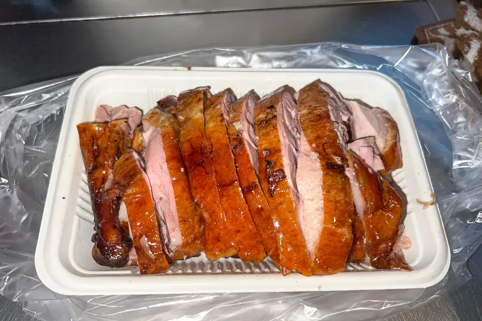 Pato asado cortado en tajadas, con piel dorada y carne rosada, en una bandeja