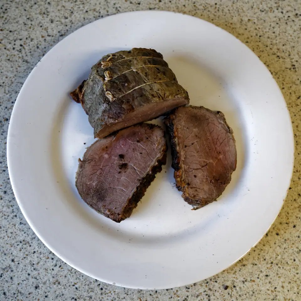 Pieza de carne vacuna magra asada, cortada en rodajas gruesas, en un plato blanco