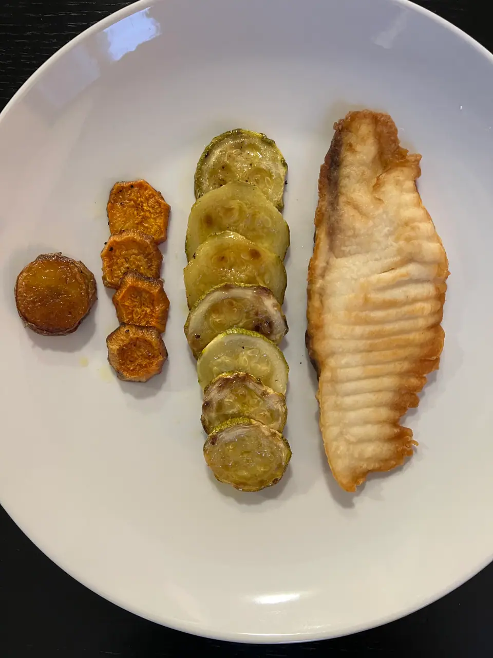 Filete de pescado blanco cocido en un plato, junto a rodajas de zapallito y boniato asados