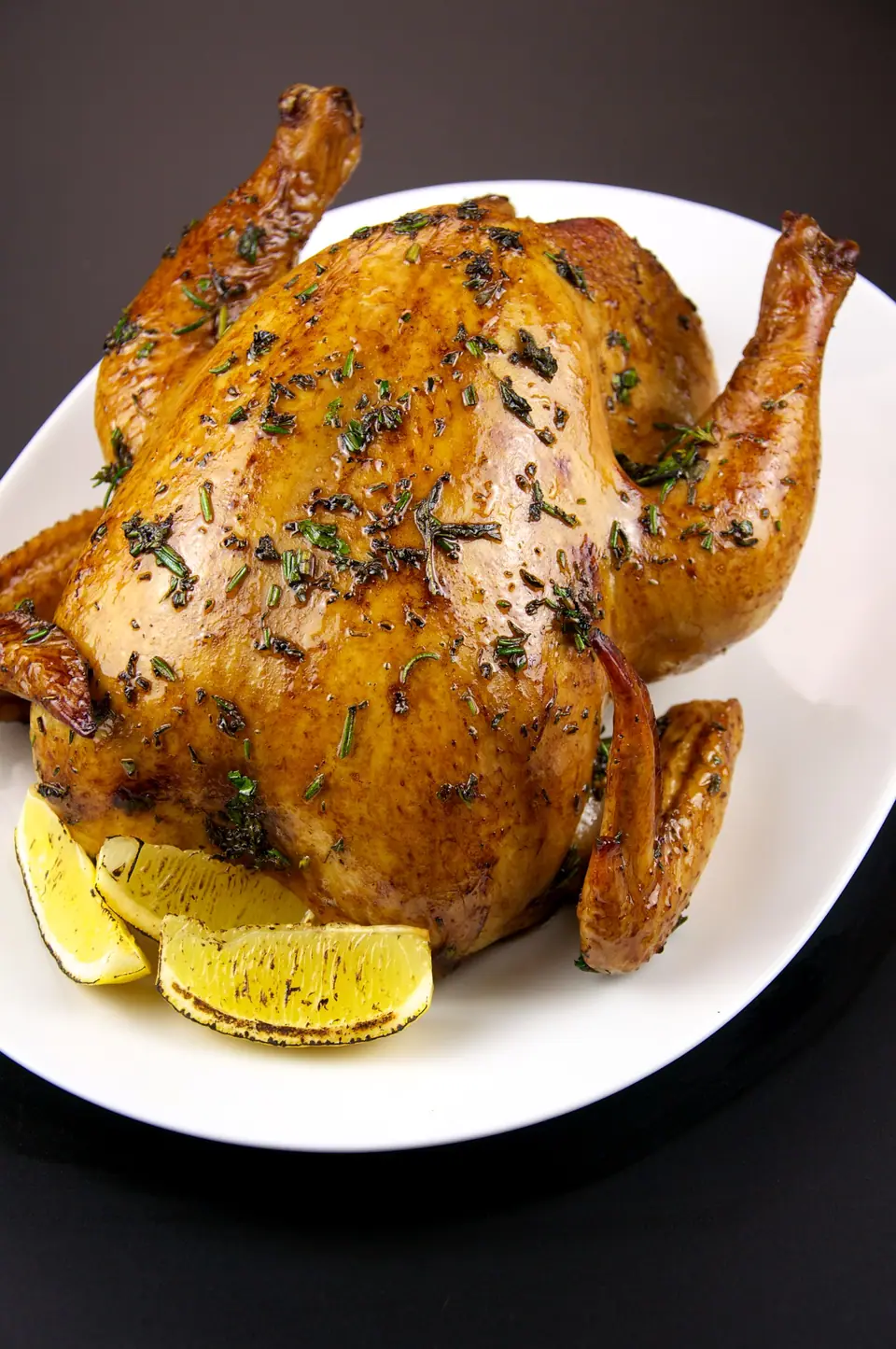 Pollo entero asado con hierbas, servido en una fuente con limón