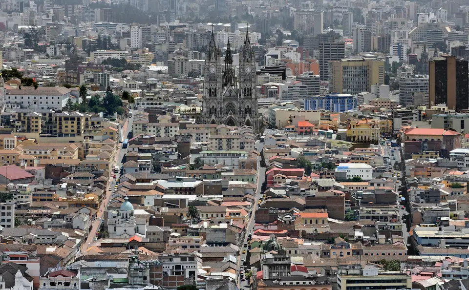 Vista aérea del centro de Quito con una basílica gótica entre edificios y cerros al fondo