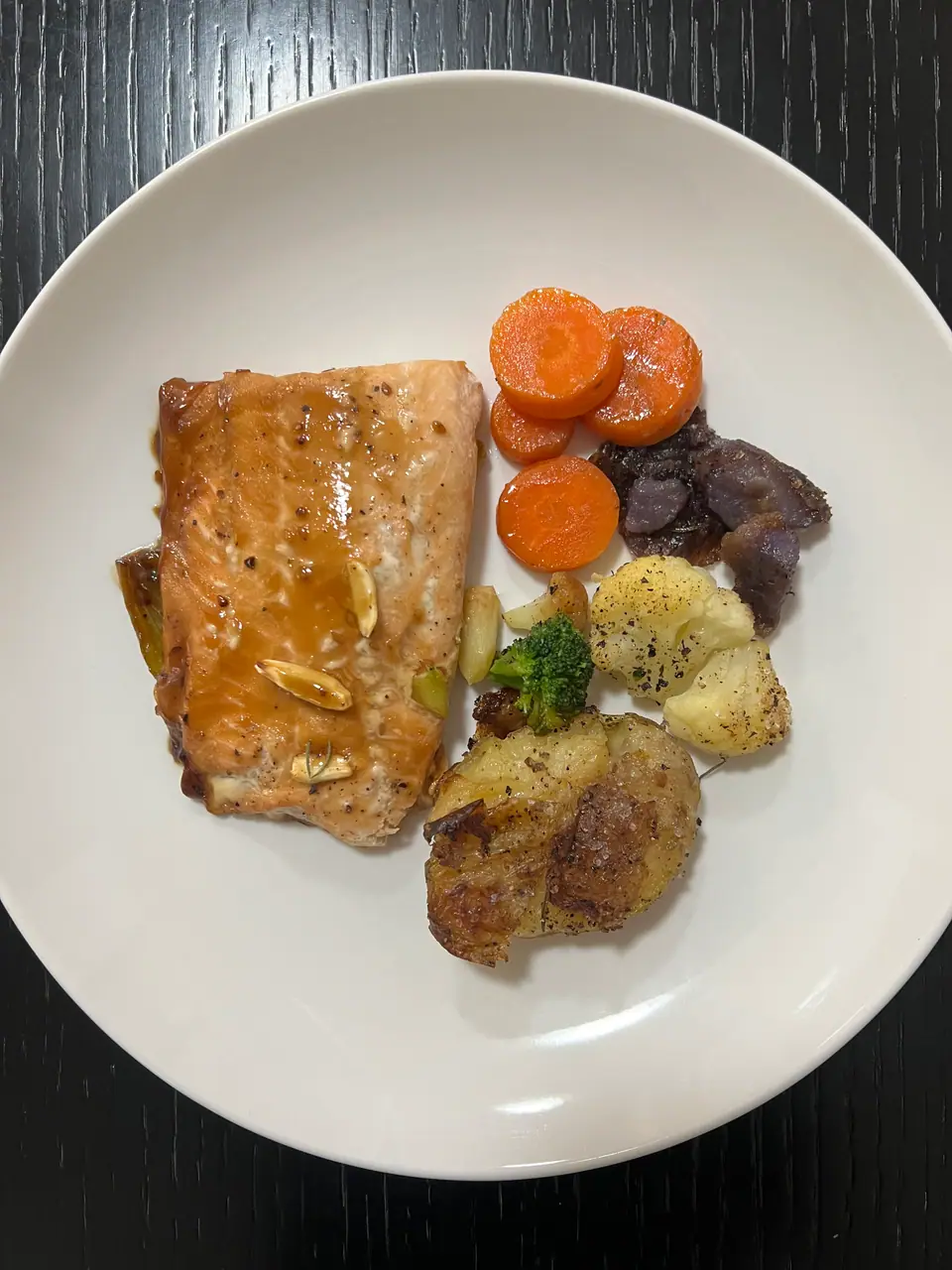 Filete de salmón al horno en un plato blanco con zanahorias, papas y verduras
