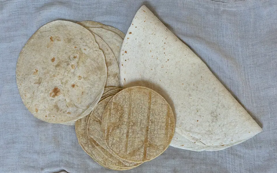 Tortillas de maíz y de harina de trigo apiladas sobre un mantel blanco
